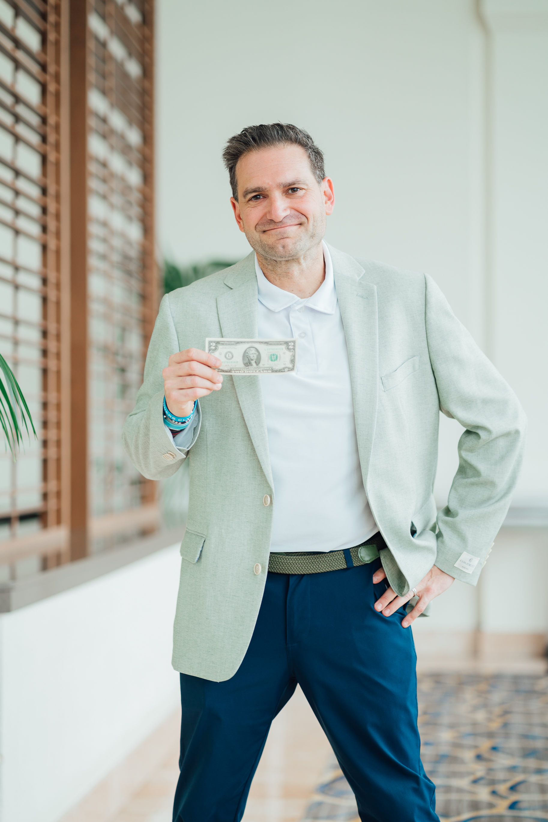 Brad Holcman in a sage blazer holding up a real two dollar bill